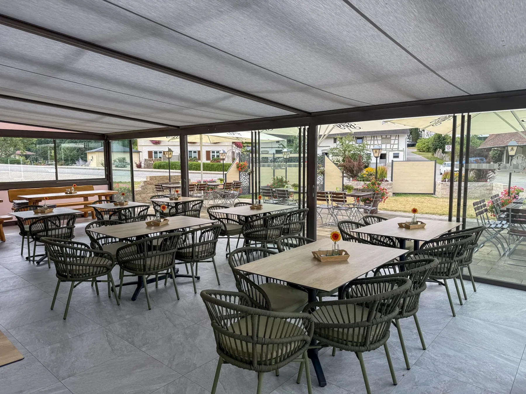 Wintergarten des Gasthaus Löwen: gedeckte Tische mit Korbsesseln hinter raumhohen Glasfronten, dahinter die Terrasse